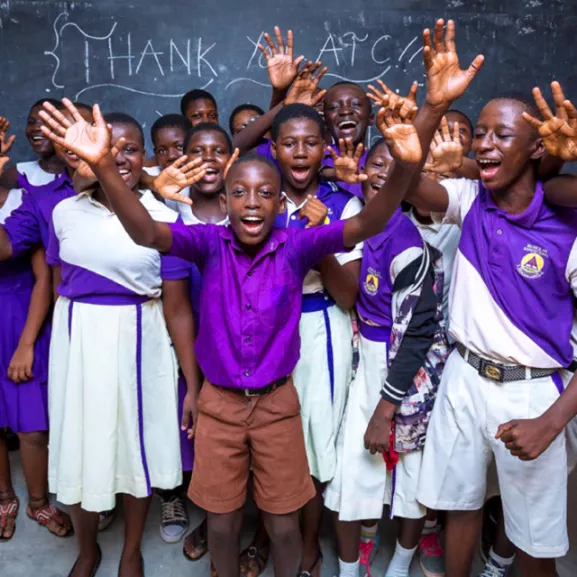 Elementary school students cheering for photo, in front of a chalkboard