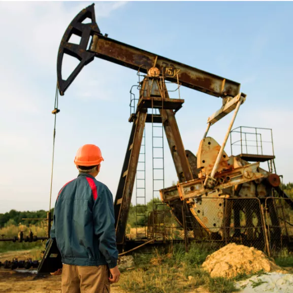 Engineer wearing orange helmet checking the pumpjack in the oil well of the oil field at the sunset.