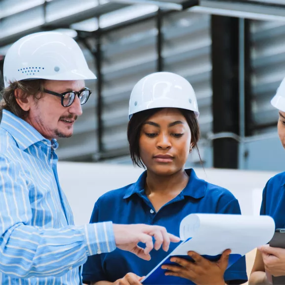 Three people in hard hats examining a blueprint, discussing plans for a construction project.