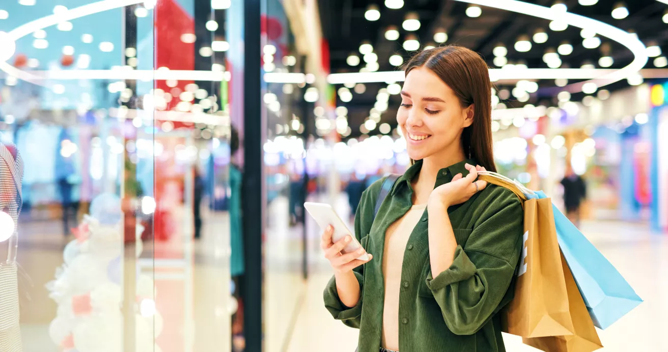 A woman with shopping bags checking her phone.